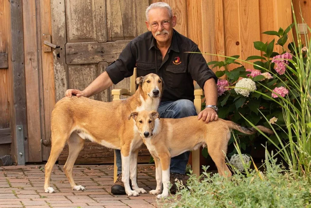 Ein Mann sitzt mit zwei Hunden in einem Garten.