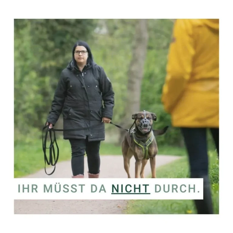 Frau mit Hund an der Leine im Park, Hund trägt Maulkorb.