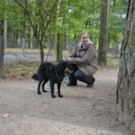 Eine Frau kniet neben ihrem Hund in einem Wald.