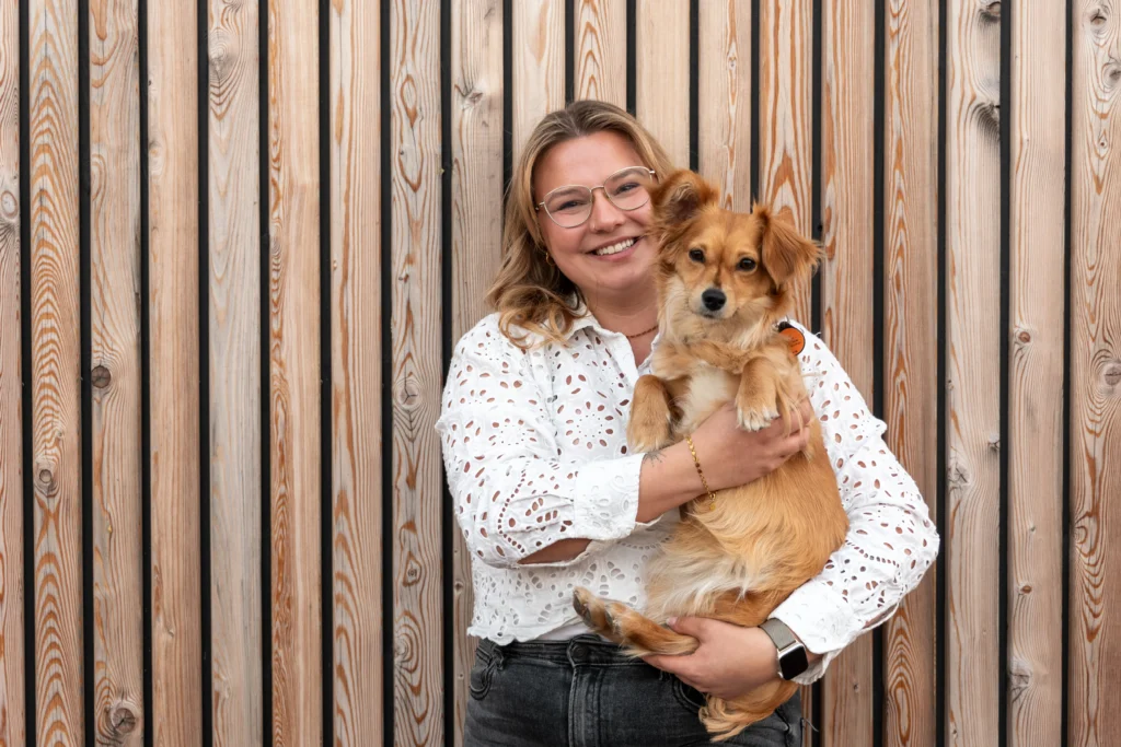 Eine Frau hält einen Hund vor einer Holzlattenwand.