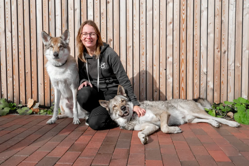 Eine Frau sitzt mit zwei Wolfshunden im Garten.